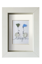 Cuadro de vidrio de mar y tinta en el que dos Pájaros posados encima del texto amigos se intercambian sedos globos con forma de corazón