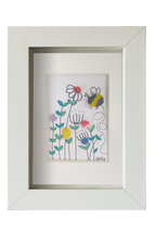 Cuadro de vidrio de mar sobre tinta y acuarela con un abejorro revoloteando entre flores silvestres de distintos colores. Marco blanco