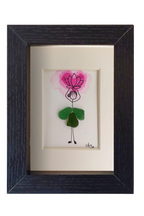 Cuadro con dibujo de chica con falda de vidrio de mar verde que sostiene sobre la cabeza una flor de loto rosada hecha con acuarela y tinta. Marco negro