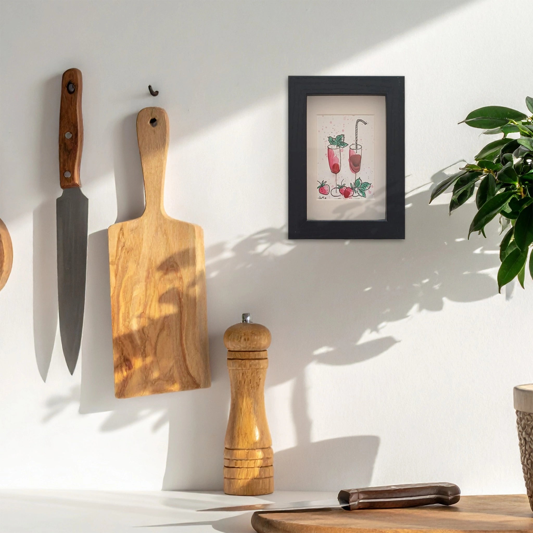 Pared de cocina con utensilios y un cuadro con dos cócteles de fresa colgados