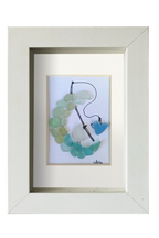 Cuadro con dibujo de Pájaro pescando un corazón encima de una media luna de vidrio de mar. Marco color blanco