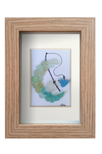 Cuadro con dibujo de Pájaro pescando un corazón encima de una media luna de vidrio de mar. Marco madera