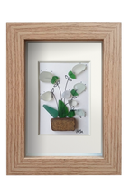 Cuadro con maceta de fragmento de cerámica y planta con flores blancas de tinta y vidrio de mar erosionado