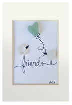 Dos pajaritos de vidrio de mar se intercambian un globo en forma de corazón posados sobre la palabra friends