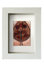 Cuadro de tinta, acuarela y vidrio de mar marrón representando una hoja otoñal. Marco blanco