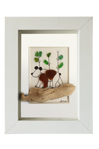 Cuadro con un fragmento de madera desgastado a modo de camino y un oso dibujado en tinta y vidrio de mar marrón, andando por un bosque adornado con vidrios verdes. Marco blanco