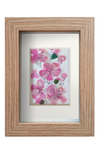 Cuadro con delicadas flores de acuarela rosa y tinta con vidrio de mar translúcido dándo volumen y vida a los pétalos. 3 capullos de vidrio verde le dan contraste a las flores rosa. Marco madera