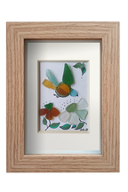 Cuadro de vidrio de mar y tinta con un pajaro multicolor volando hacia unas flores. Marco madera