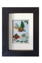 Cuadro de vidrio de mar y tinta con un pajaro multicolor volando hacia unas flores. Marco negro