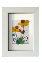 Cuadro de vidrio de mar y tinta con una planta con flores amarillas de centro marrón y hojas verdes. Marco Blanco