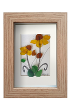 Cuadro de vidrio de mar y tinta con una planta con flores amarillas de centro marrón y hojas verdes