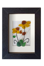 Cuadro de vidrio de mar y tinta con una planta con flores amarillas de centro marrón y hojas verdes. Marco negro